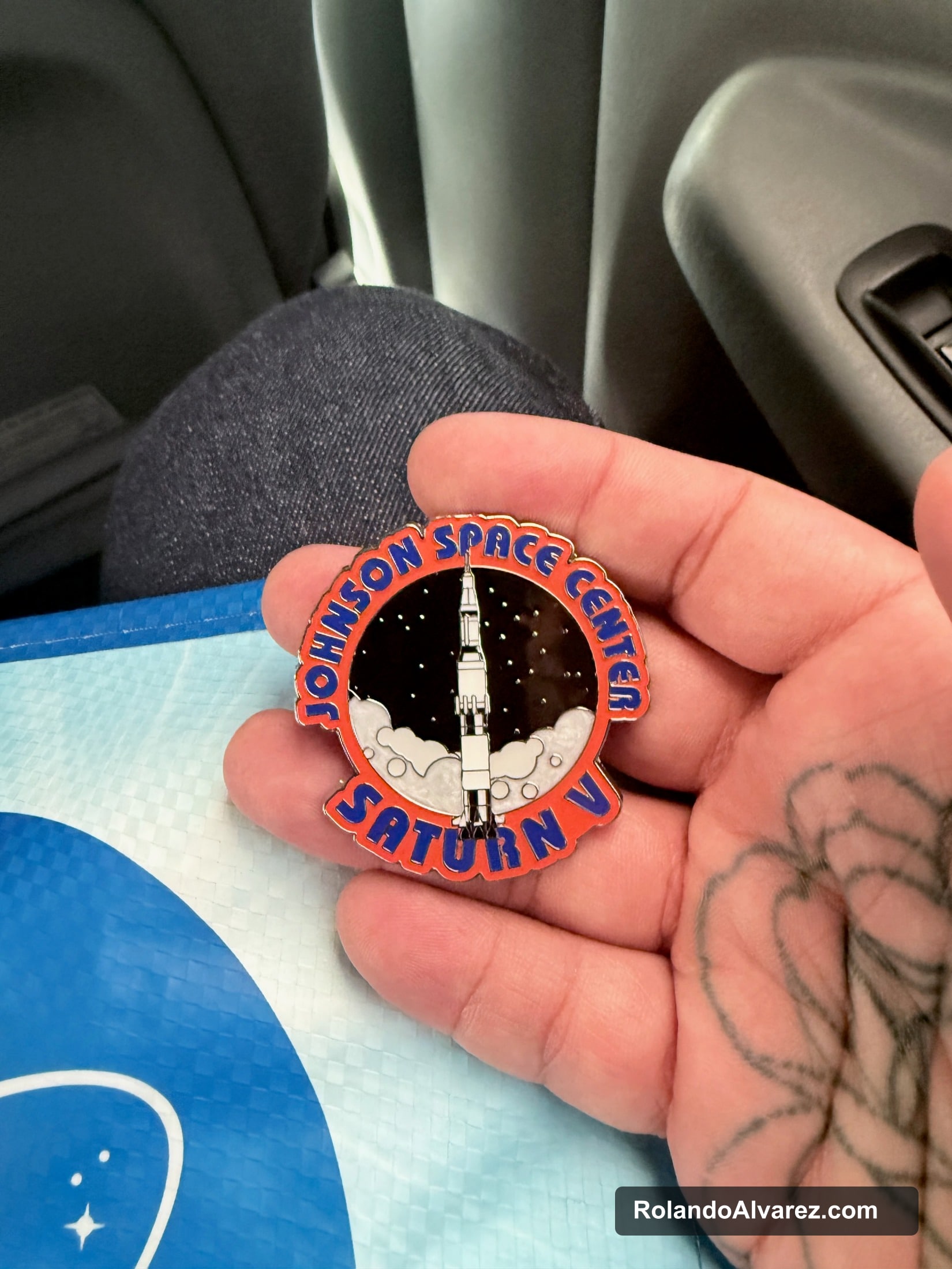 A Johnson Space Center Saturn V souvenir pin held in one hand
